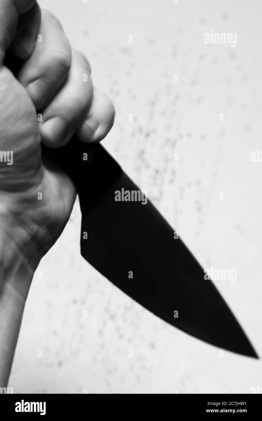 Vertical grey scale shot of a person holding a black knife with a white ...