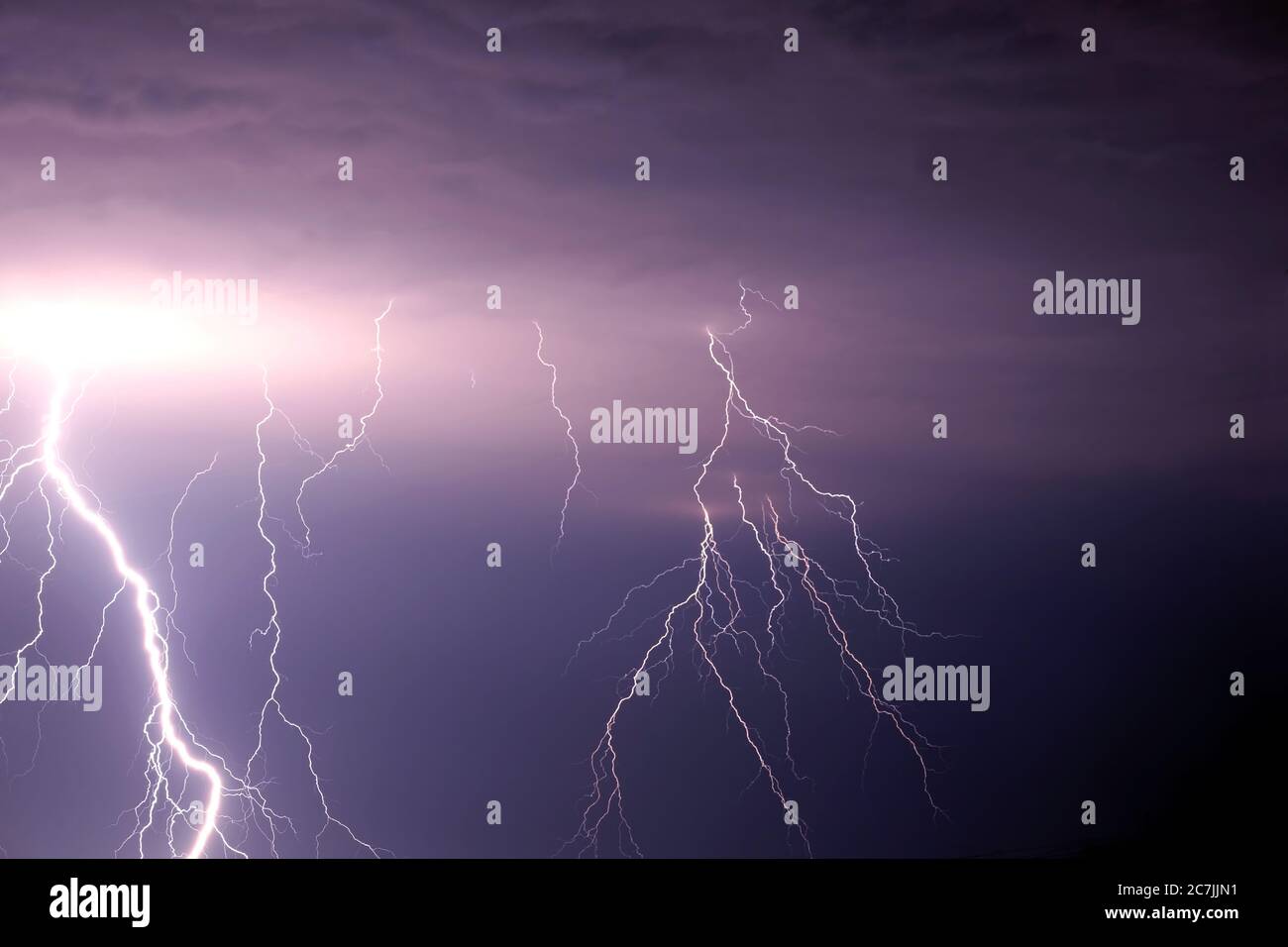 Many bright lightning discharges in the stormy sky under heavy purple rain clouds Stock Photo