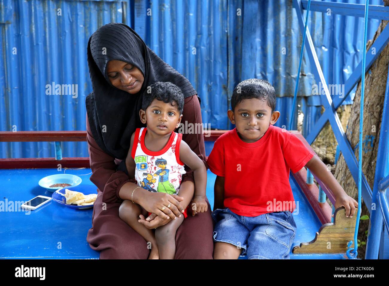 Mujer musulmana con sus dos hijos al atardecer jugando en un patio de recreo en la isla de Guraidhoo, Maldivas Stock Photo