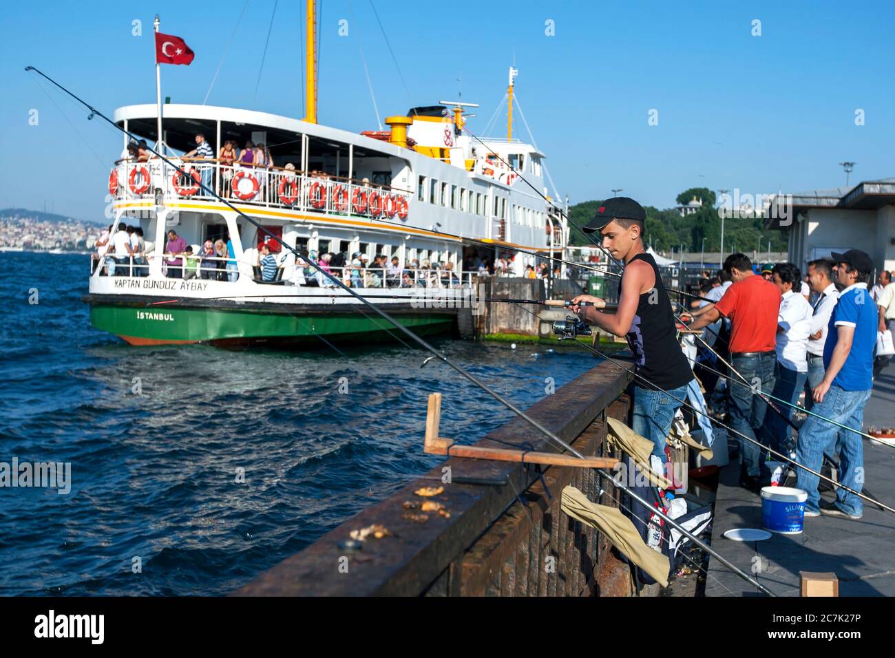 Fishermen cast their lines into Golden Horn at Eminonu in Istanbul in Turkey. In the background is one of the many passenger ferry boats. Stock Photo