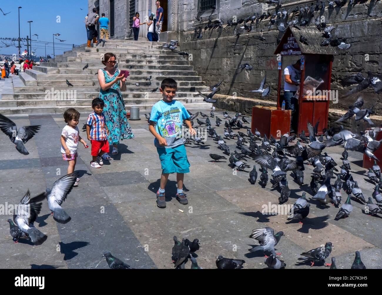 Children try to catch pigeons gathered next to the 400 year old Yeni Camii in the Eminonu district of Istanbul in Turkey. Stock Photo