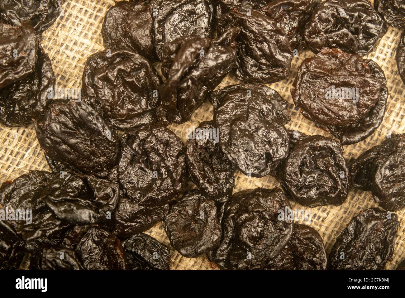 Dried prunes in bulk on burlap with a rough texture. Close up Stock