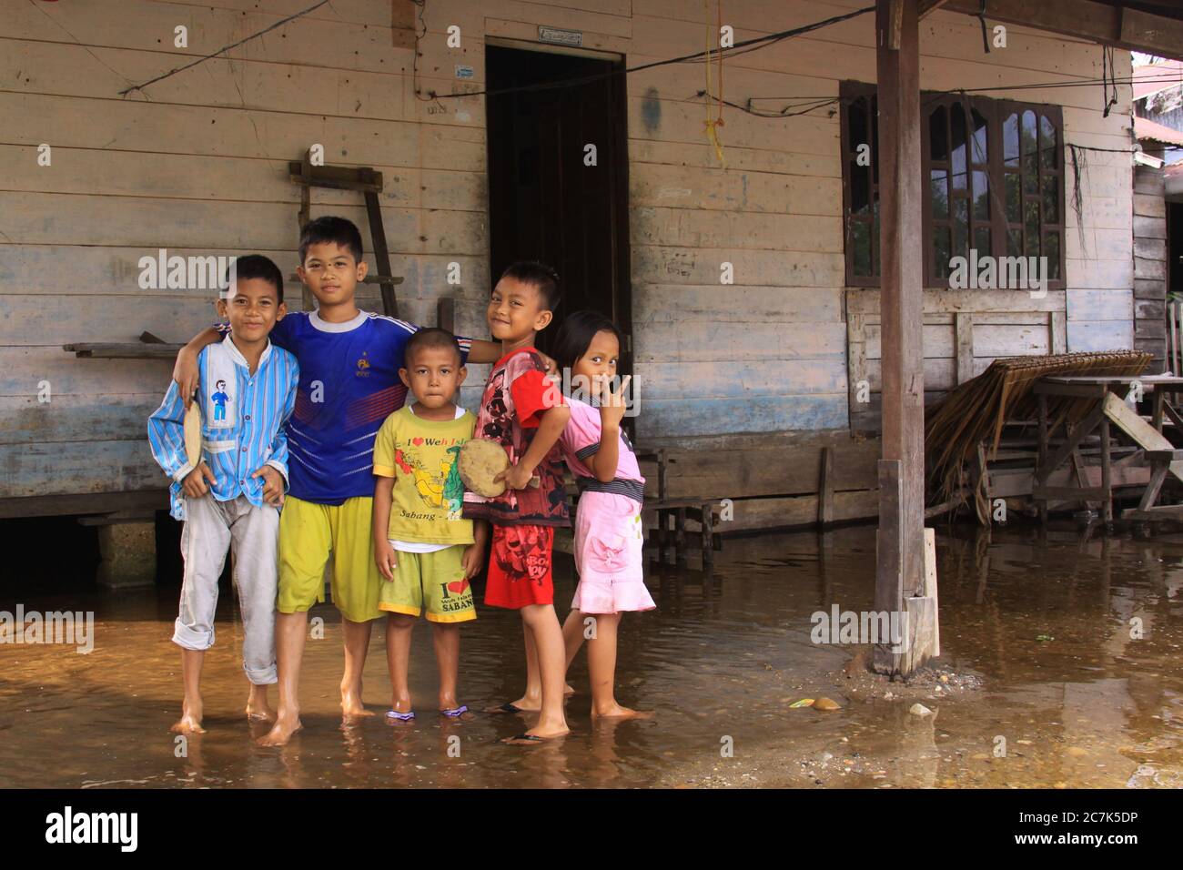 Playful children in colorful clothes, posing in front of wooden house flooded by Alas river waters, in Singkil, Aceh, Indonesia. Stock Photo