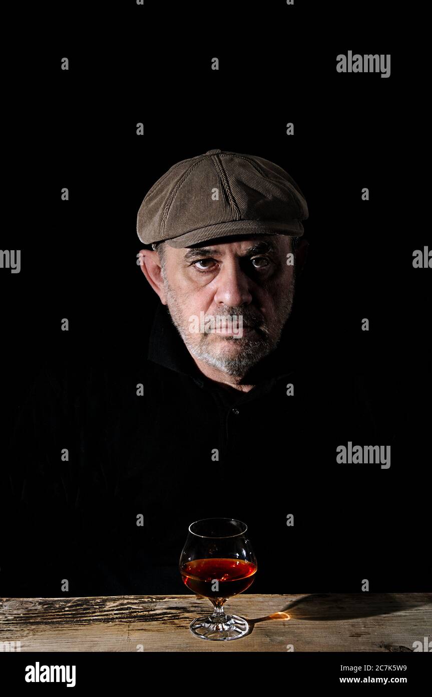 An elderly man in a cap sits at a table in front of a glass of wine Stock Photo