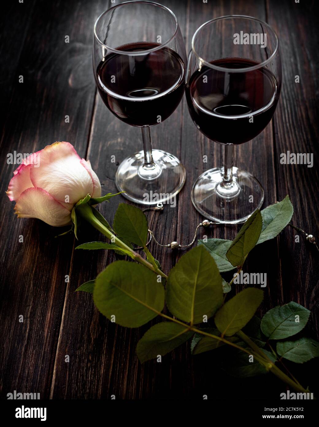 Two glasses of red wine and a rose located on a vintage wooden table Stock Photo