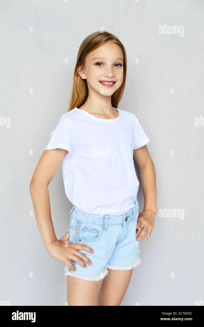 Young sportive girl in white t-shirt and jeans shorts posing in studio ...