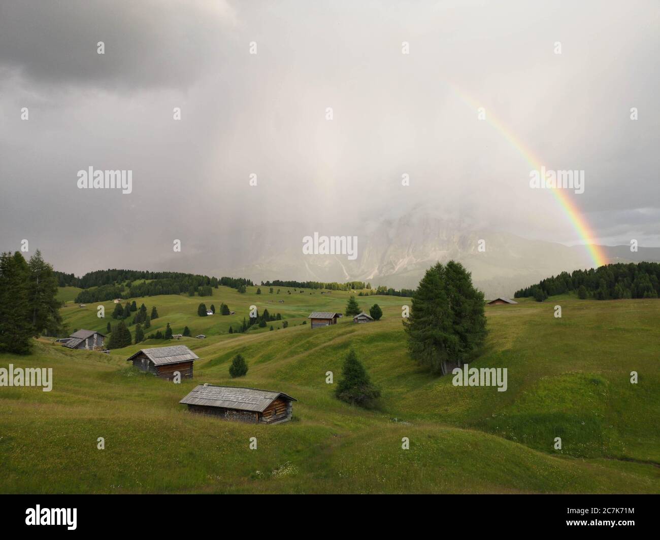 Gentle hilly landscape with huts, rainbows and mountains in the rain ...