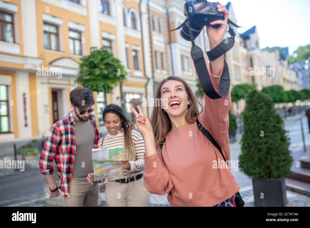 Happy girl with camera taking selfie friends at distance Stock Photo