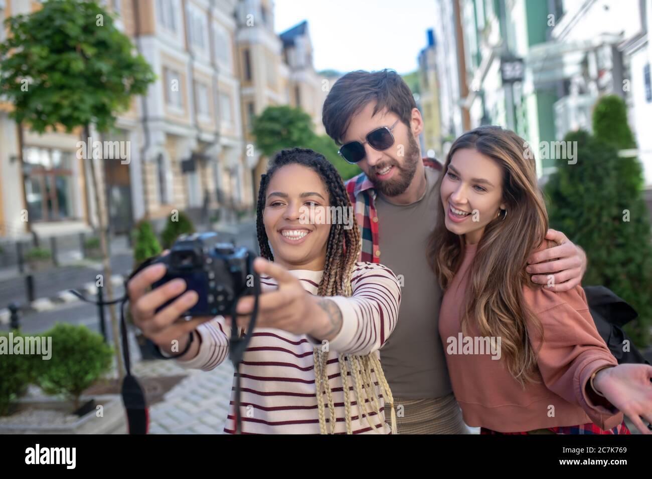 Girl with dreadlocks taking selfie on camera with friends in city. Stock Photo