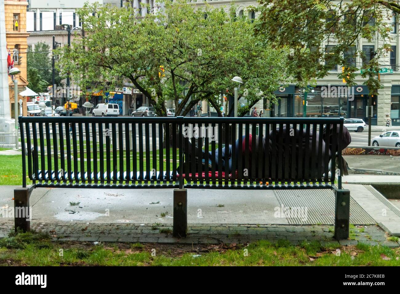 Vancuver, Canada - September 13, 2010: A homeless person rests on a city bench in downtown Vancouver, Canada. Stock Photo
