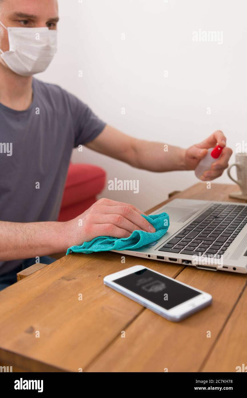 Symbol, corona virus, pandemic, man with face mask, home office, laptop, keyboard, cleaning, disinfection Stock Photo