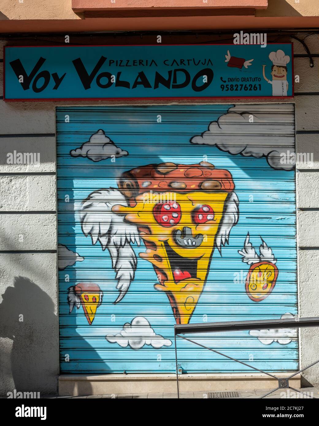 A cartoon pizza-slice cherub face advertises the Voy Volando pizzeria in Calle Real de Cartuja, Granada Stock Photo