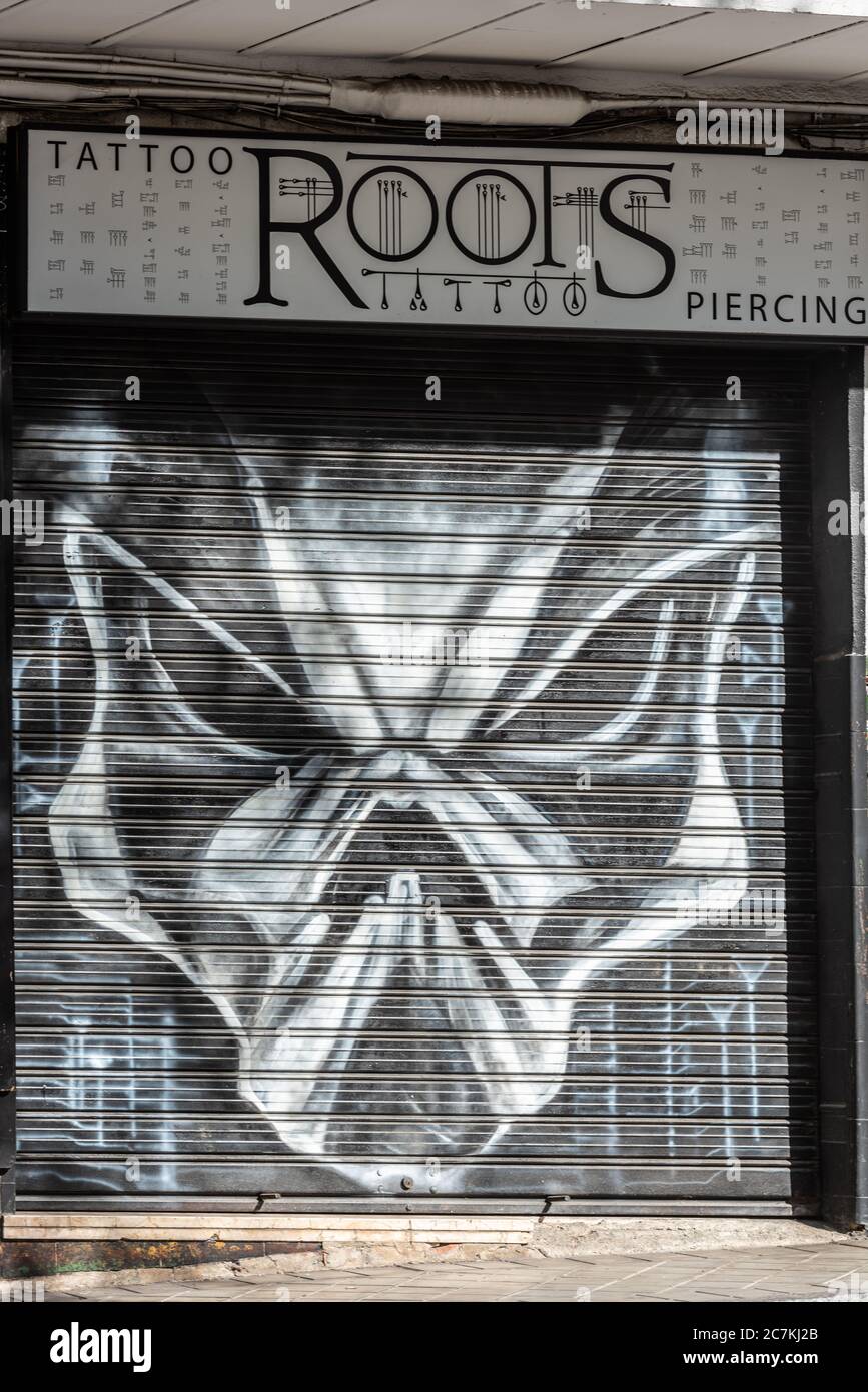 An ominous looking alien face looks out from the shutters of the Roots Tattoo parlour in Cuesta de San Antonio, Granada Stock Photo
