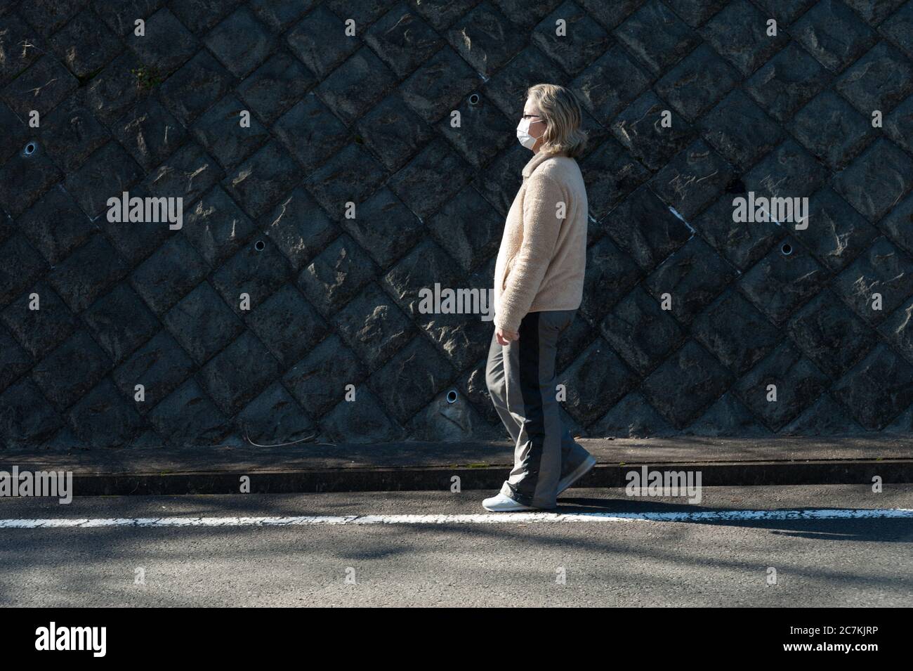 Woman 40-49 years walking outdoors, wearing glasses and white mask for protection against coronavirus (COVID-19) and other infectious diseases. Stock Photo