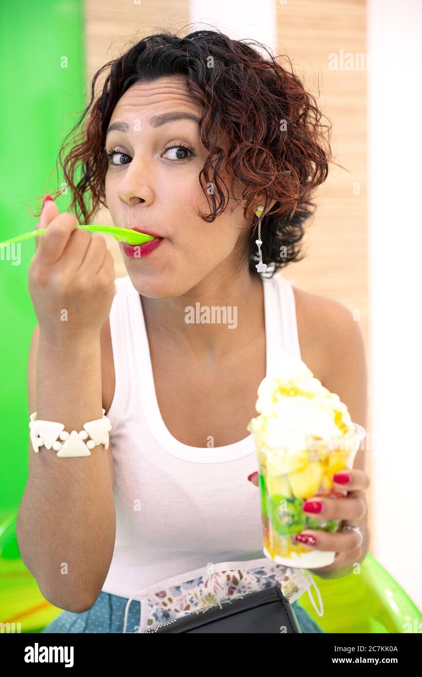 Portrait of a young, brown-skinned woman savoring an ice cream. Selective focus. Summer and healthy lifestyle concept. Stock Photo