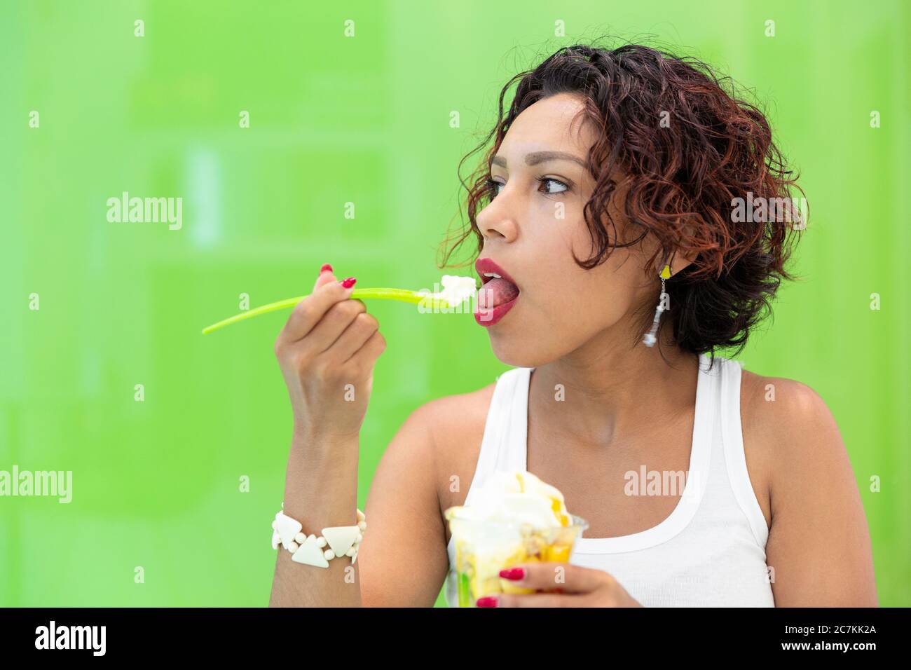 Close-up of Latin girl having ice cream on a green background. Space for text. Selective focus. Summer and healthy lifestyle concept. Stock Photo