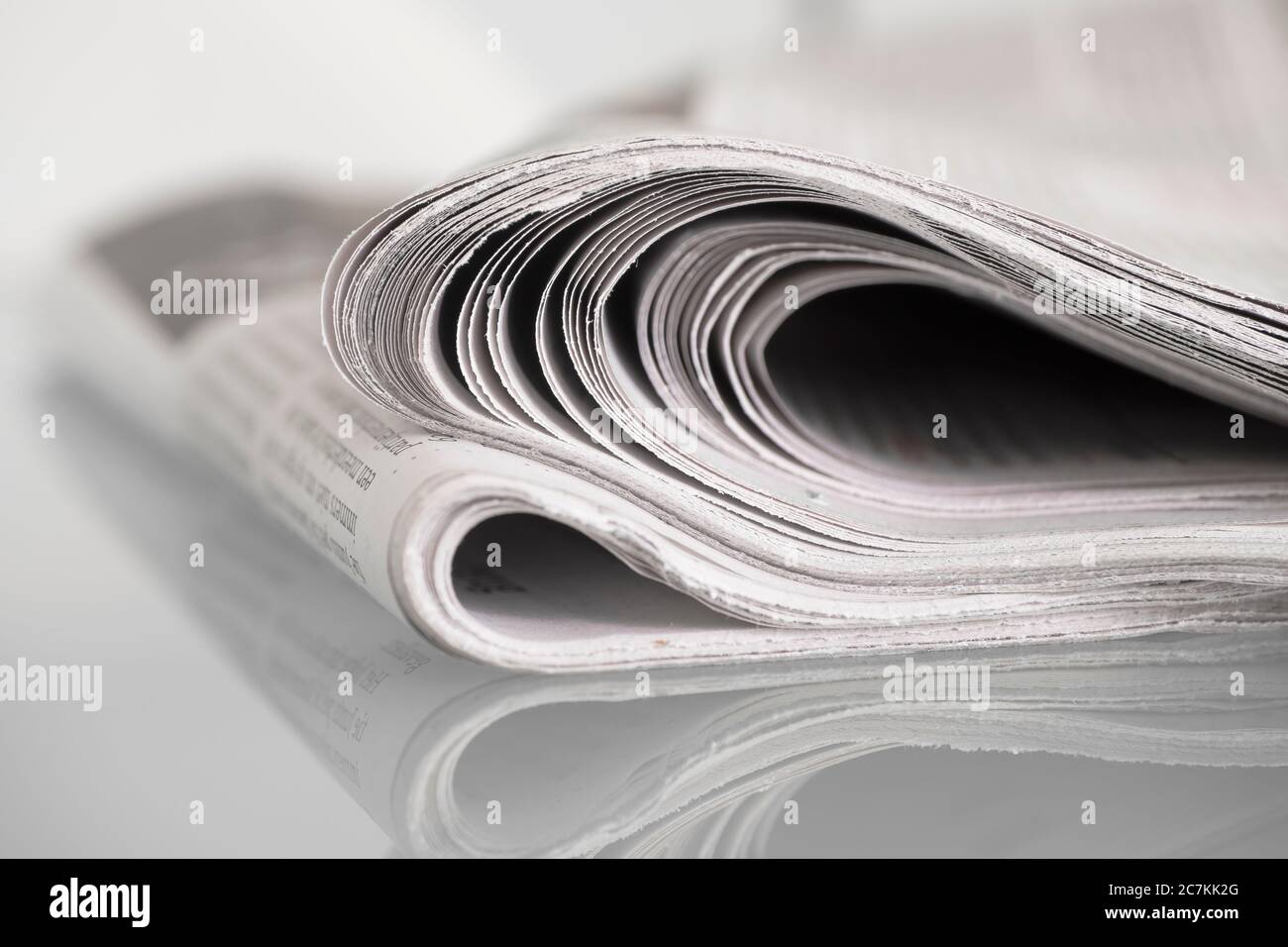 Folded newspaper mirrored on glass table against plain background with narrow depth of field Stock Photo
