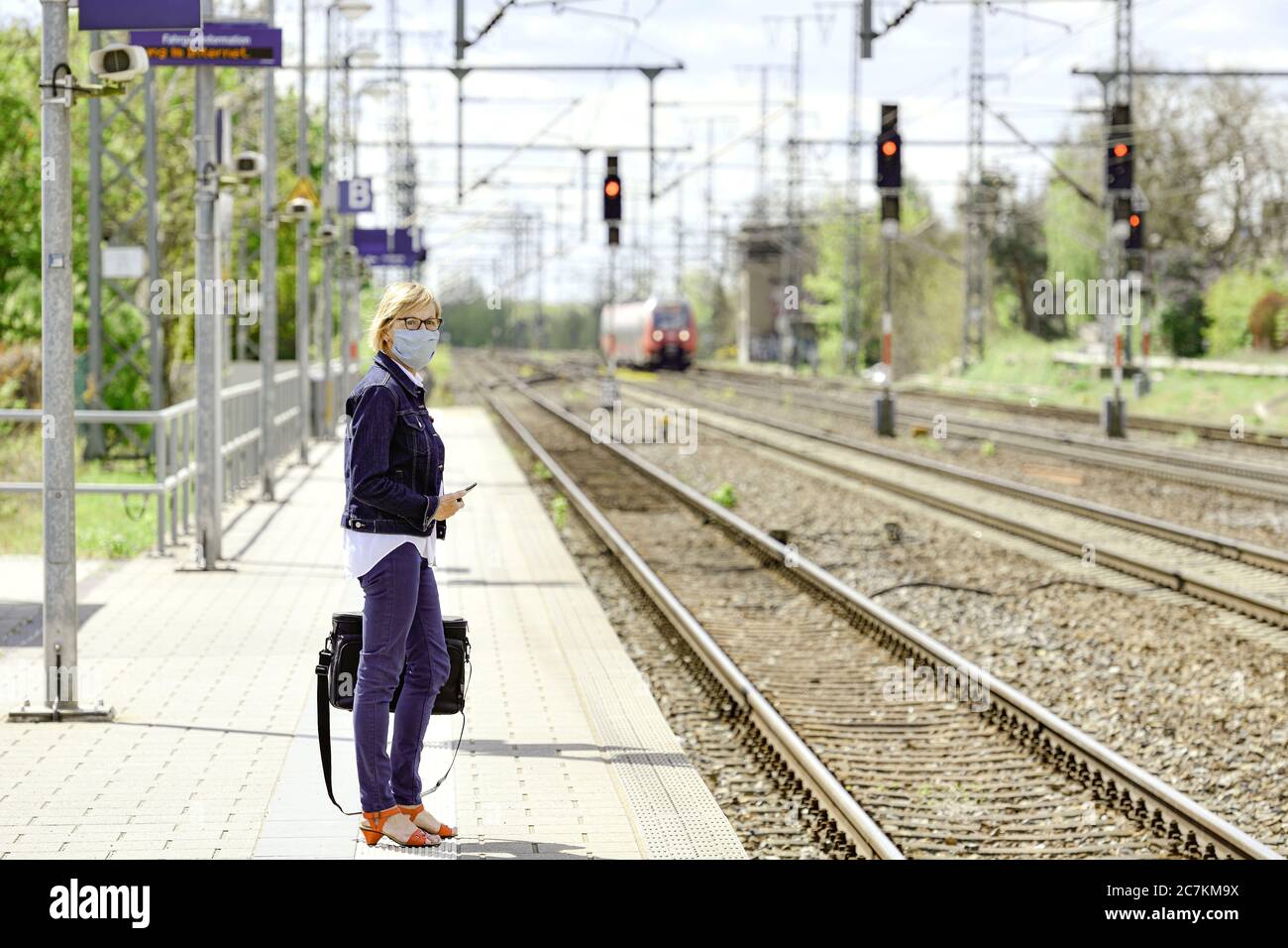 Woman with self-sewn mouth-nose guard and briefcase stands on the platform and waits for the train Stock Photo