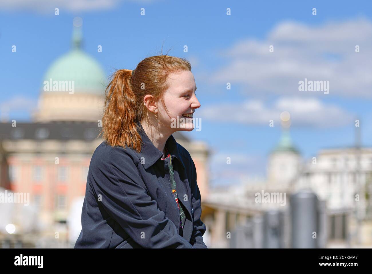 Young girl with reddish hair sits outside and smiles, portrait, sideways Stock Photo