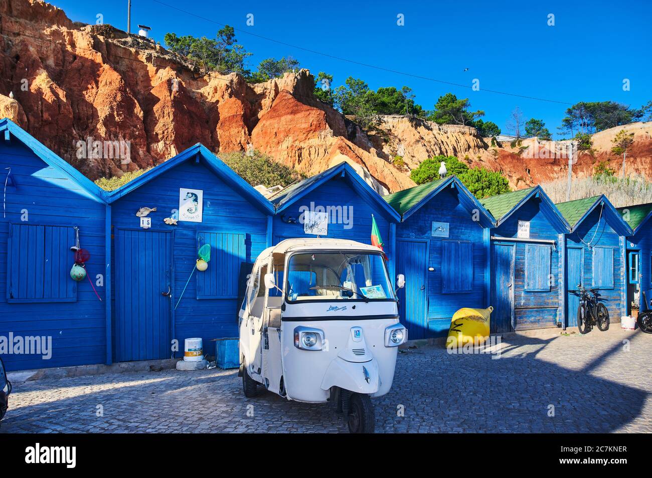Europe, Portugal, Algarve, Litoral, Barlavento, Faro District, Praia dos Olhos de Agua, blue fishing huts in front of a red cliff with tuktuk Stock Photo