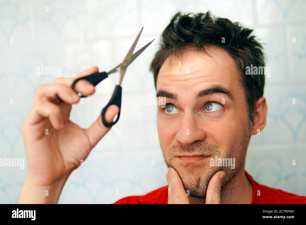 Young Man cutting his Own Hair using Scissors during Quarantine from Covid 19 - Coronavirus. fear of cutting hair. Clean yourself up on your own. Stock Photo