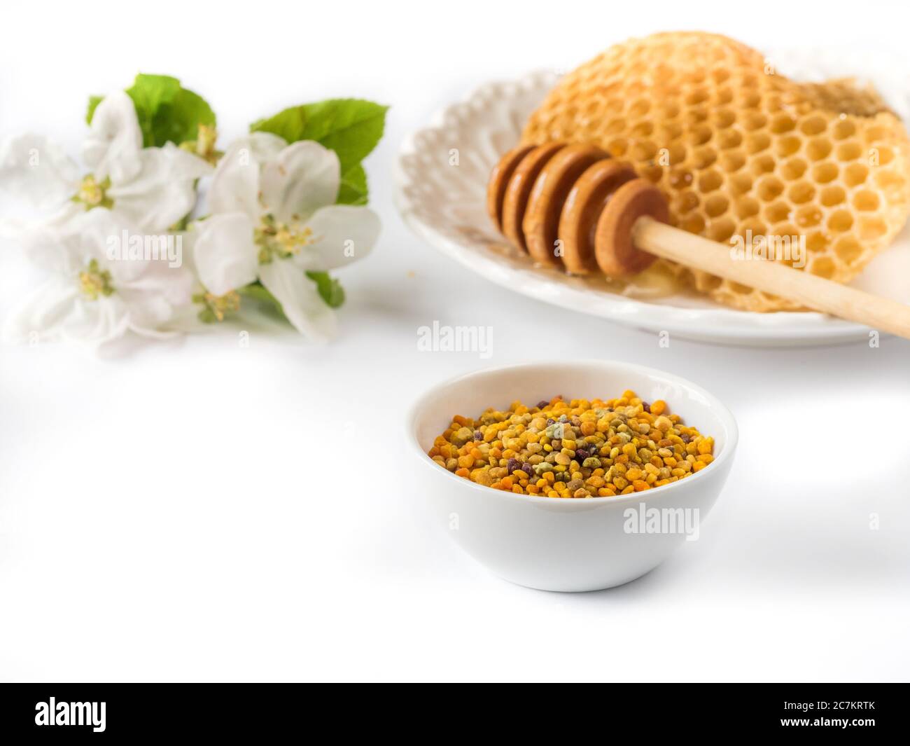 Bee pollen grains in white ceramic bowl and honeycombs on white background.  Stock Photo