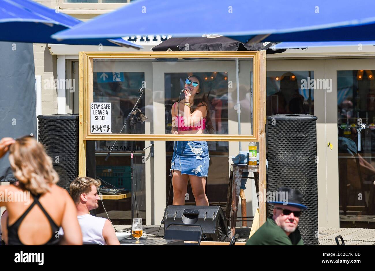 Brighton UK 18th July 2020 -  A singer performs at the Brighton Music Hall beach bar behind a screen on a beautiful sunny day on the South Coast with temperatures expected to reach the high 20s in some parts of Britain : Credit Simon Dack / Alamy Live News Stock Photo