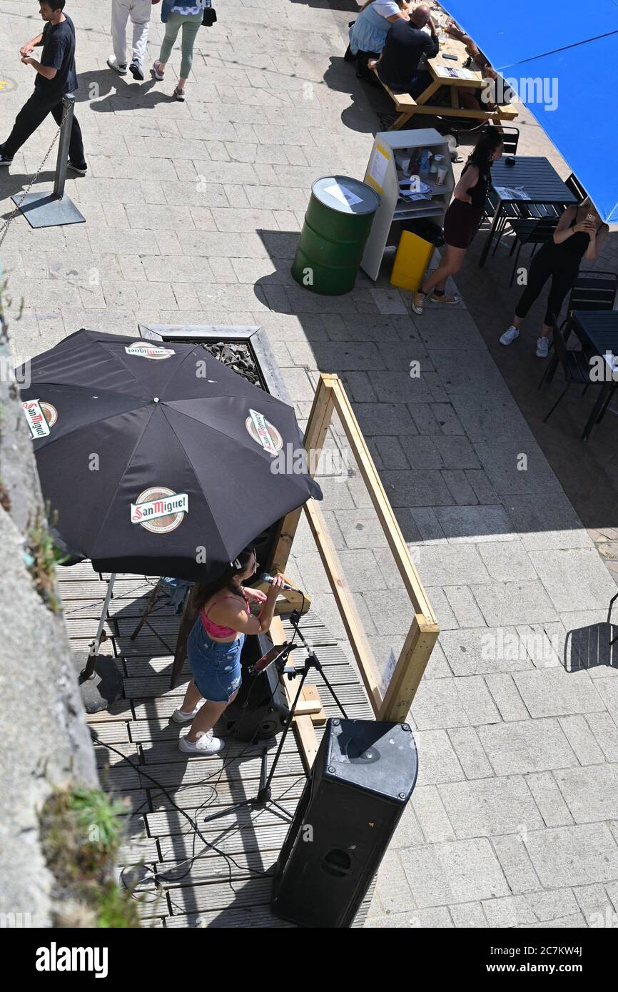 Brighton UK 18th July 2020 -  A singer performs behind a screen at the Brighton Music Hall beach bar on a beautiful sunny day on the South Coast with temperatures expected to reach the high 20s in some parts of Britain : Credit Simon Dack / Alamy Live News Stock Photo