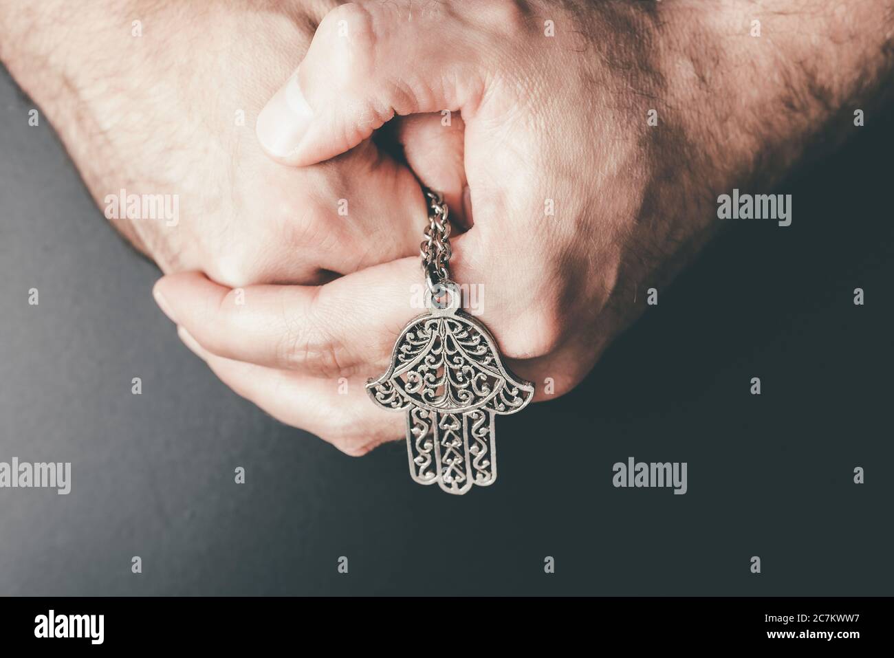 close-up of folded hands holding Hamsa amulet also known as Hand of Fatima used to protect against evil eye,, unluckiness, illness and bad fortune Stock Photo