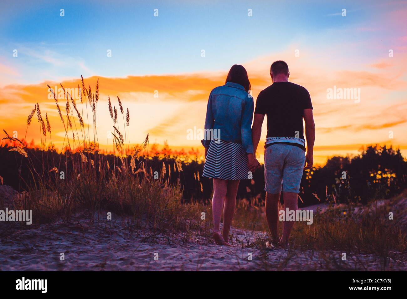 Girl And Guy Holding Hands And Standing On A Green Hill Sunset Back View Stock Photo Alamy