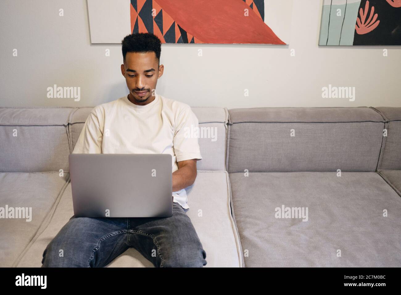 Young handsome African American guy thoughtfully working on laptop on sofa in co-working space Stock Photo