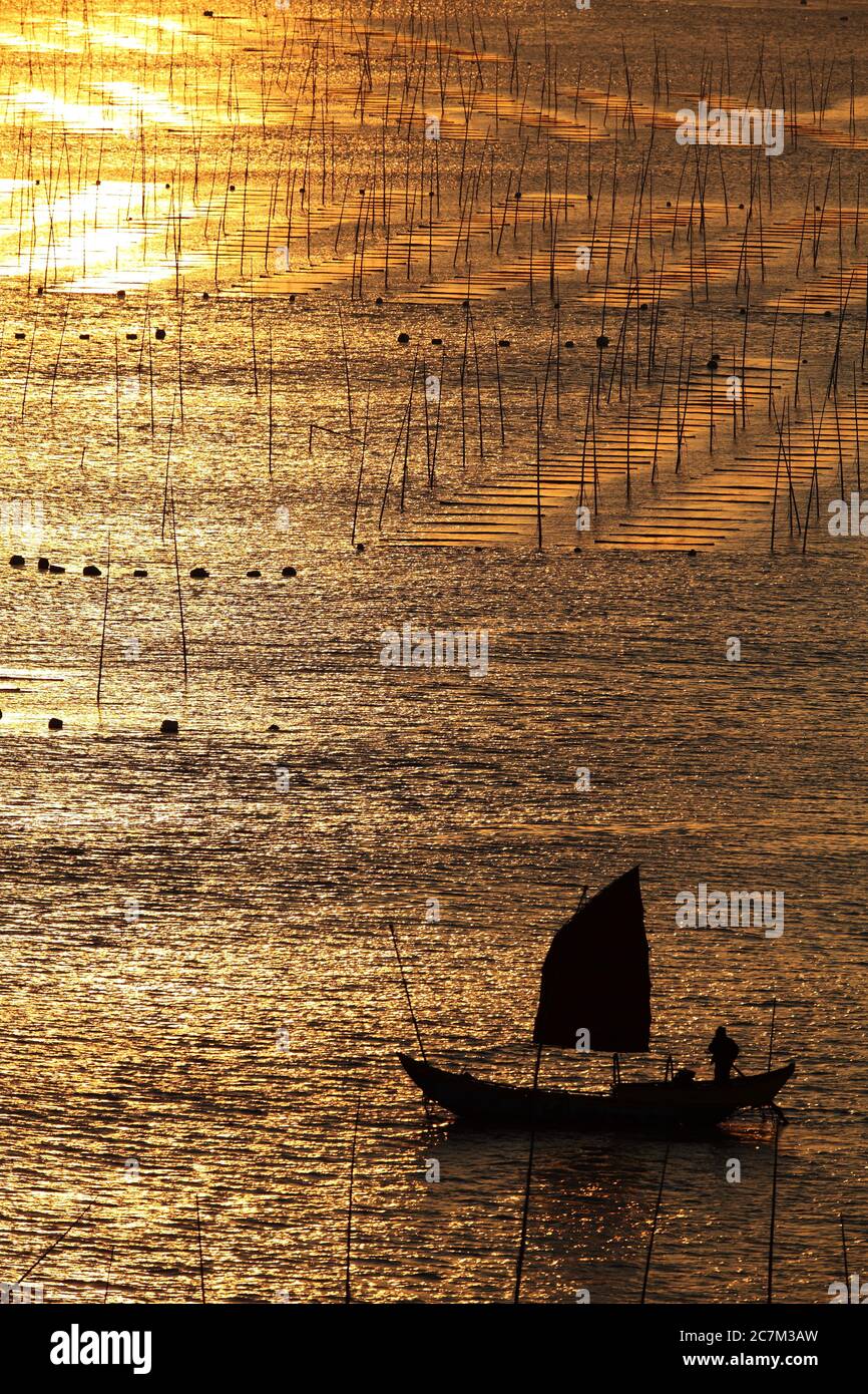 Silhouette of a sailing boat in the ocean during sunset in Xia Pu, China Stock Photo