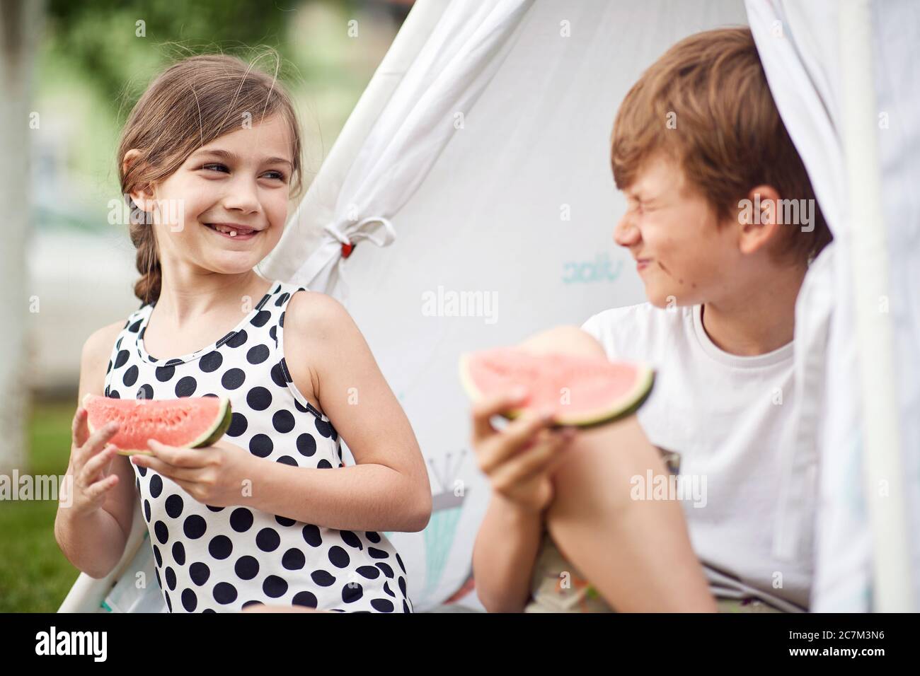 Cute  little children at backyard in teepee and eats watermelon. Stock Photo