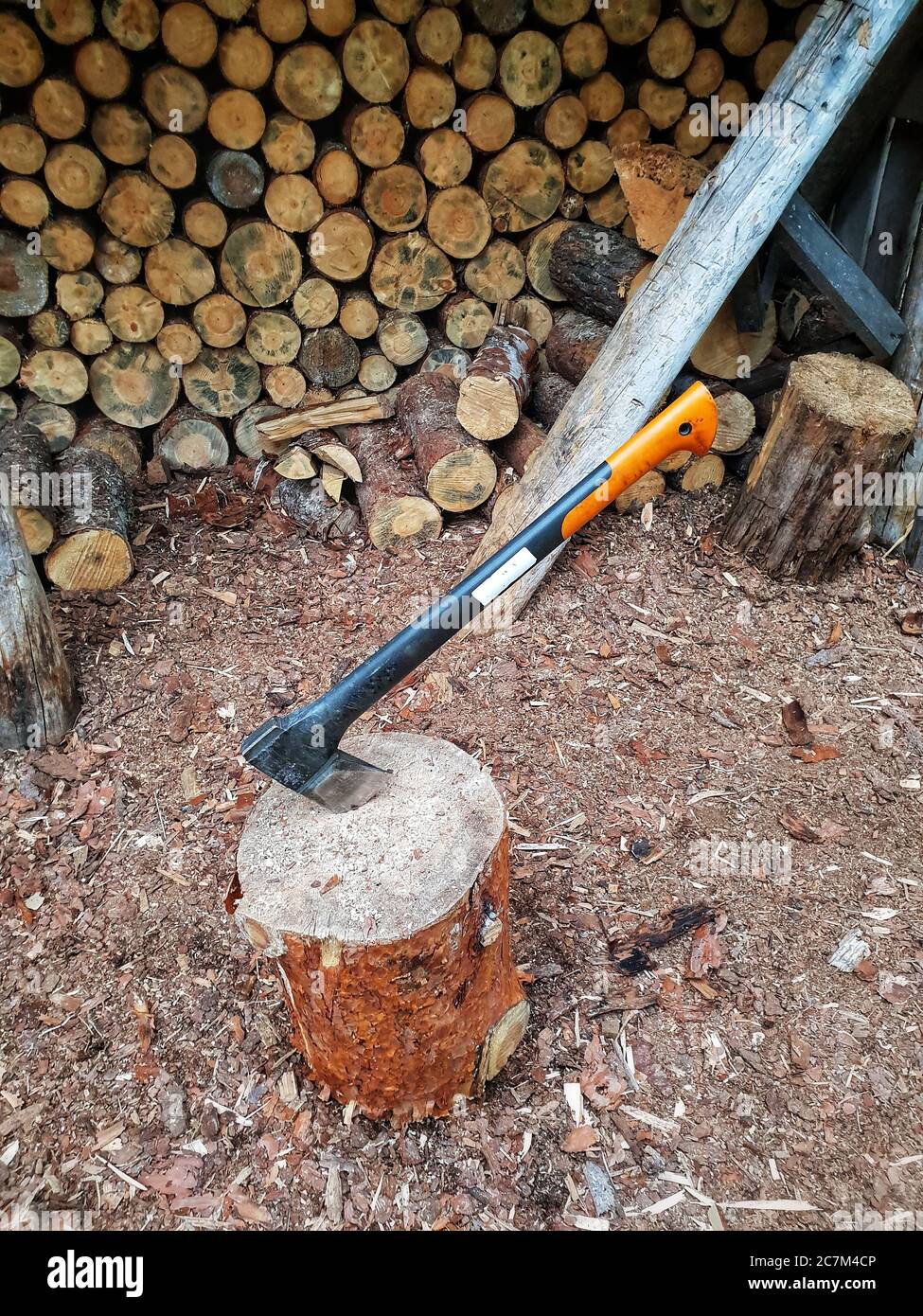 High angle shot of an axe stuck in a wood log with a pile of logs in the background Stock Photo