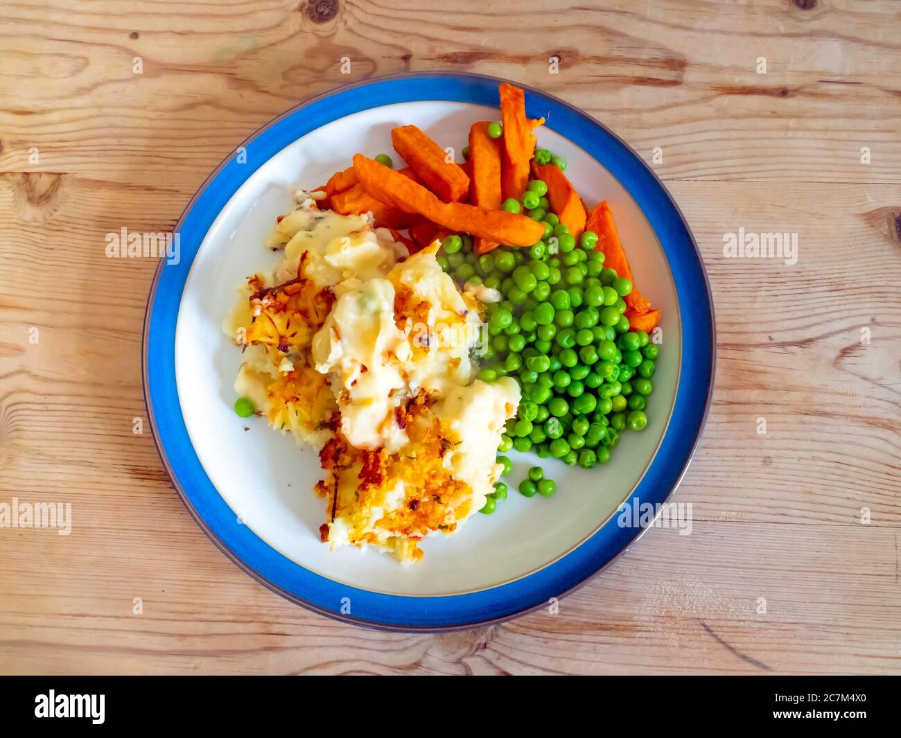 Serving of Fish Pie with garden peas and sweet potato chips on a wooden topped table Stock Photo