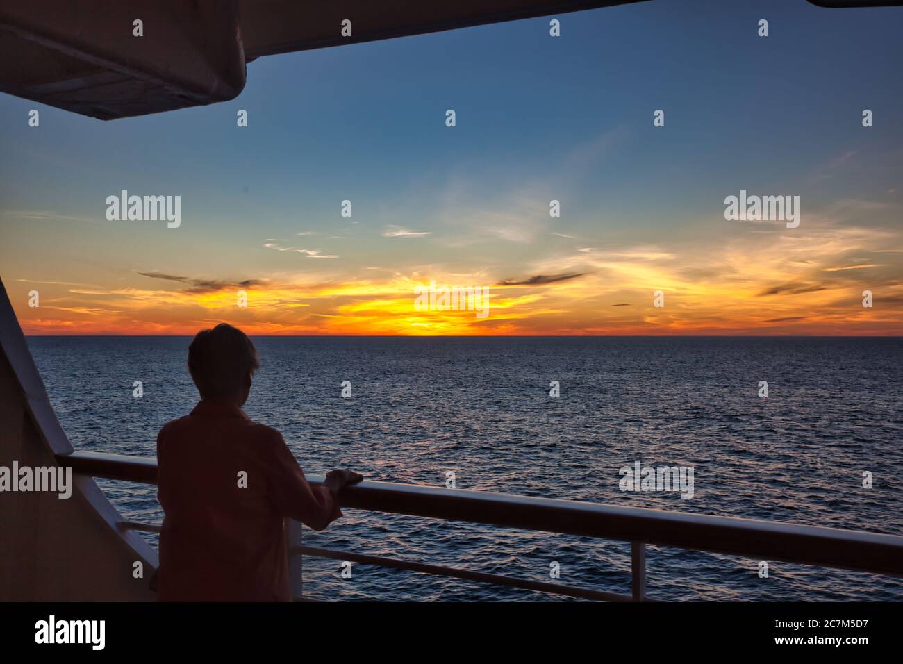 A woman at cruise ship's rail in silhouette watches a lovely sunset go down over the sea Stock Photo