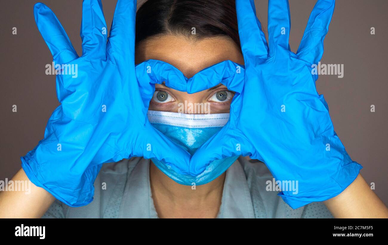 Woman with a medical mask and hands in latex glove shows the symbol of ...