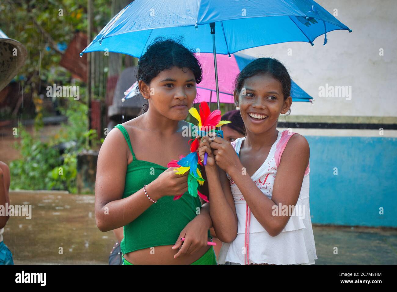 Two lovely young girls shelter under a blue umbrella from a rain shower in the town of Curua Una, in Para State, Brazil. Stock Photo