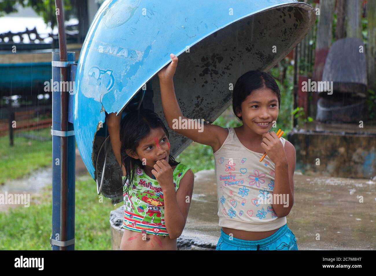 Two lovely little young girls find shelter under a phone kiosk canopy from a rain shower in the town of Curua Una, in Para State, Brazil. Stock Photo