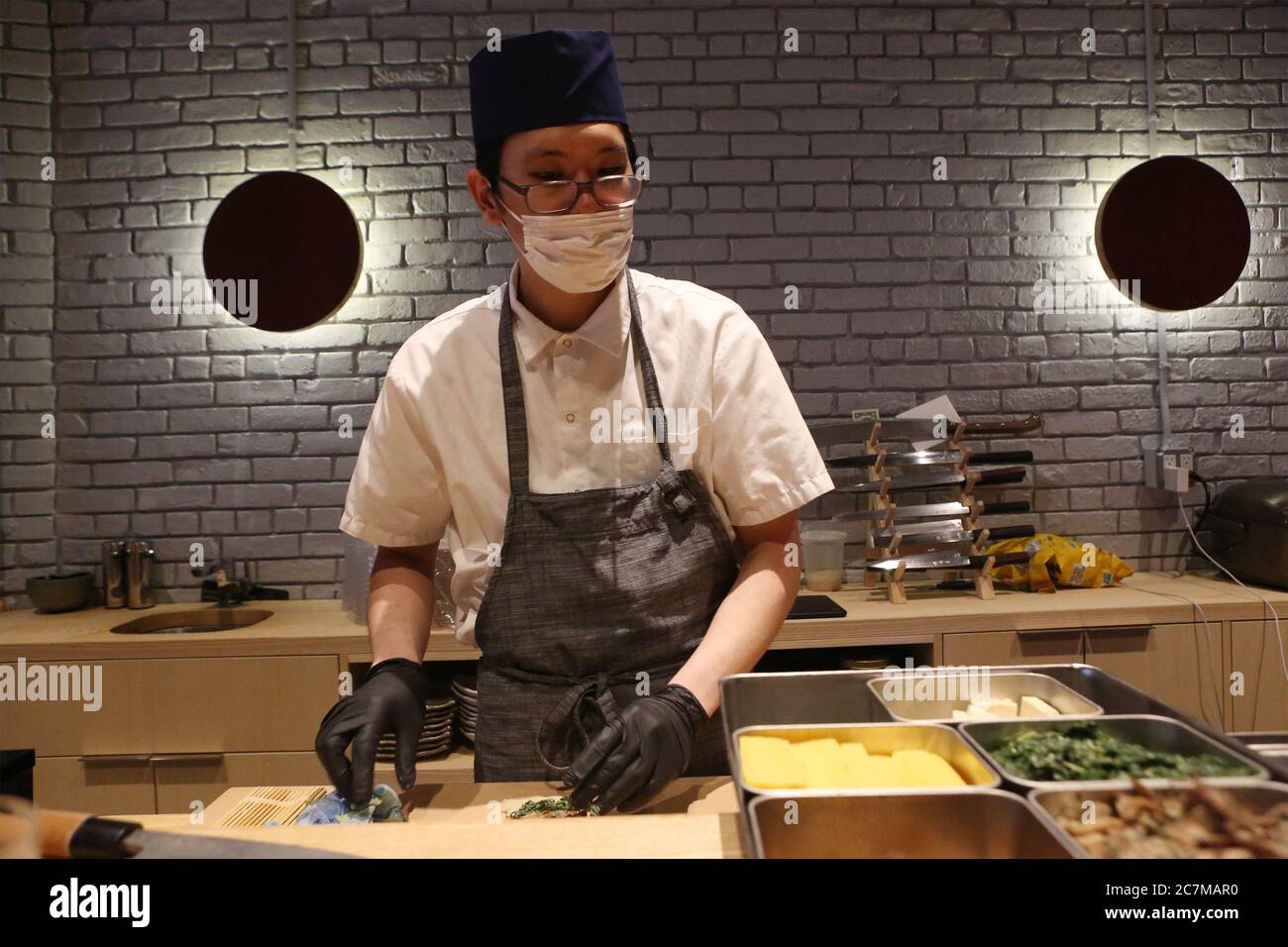 A sushi chef wearing a mask and gloves prepares food for take out and