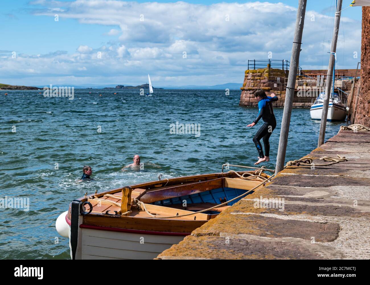 North Berwick, East Lothian, Scotland, United Kingdom, 18th July 2020. UK Weather: Summer sunshine in the seaside town. A boy jumps off the harbour wall into the Firth of Forth in West Bay Stock Photo