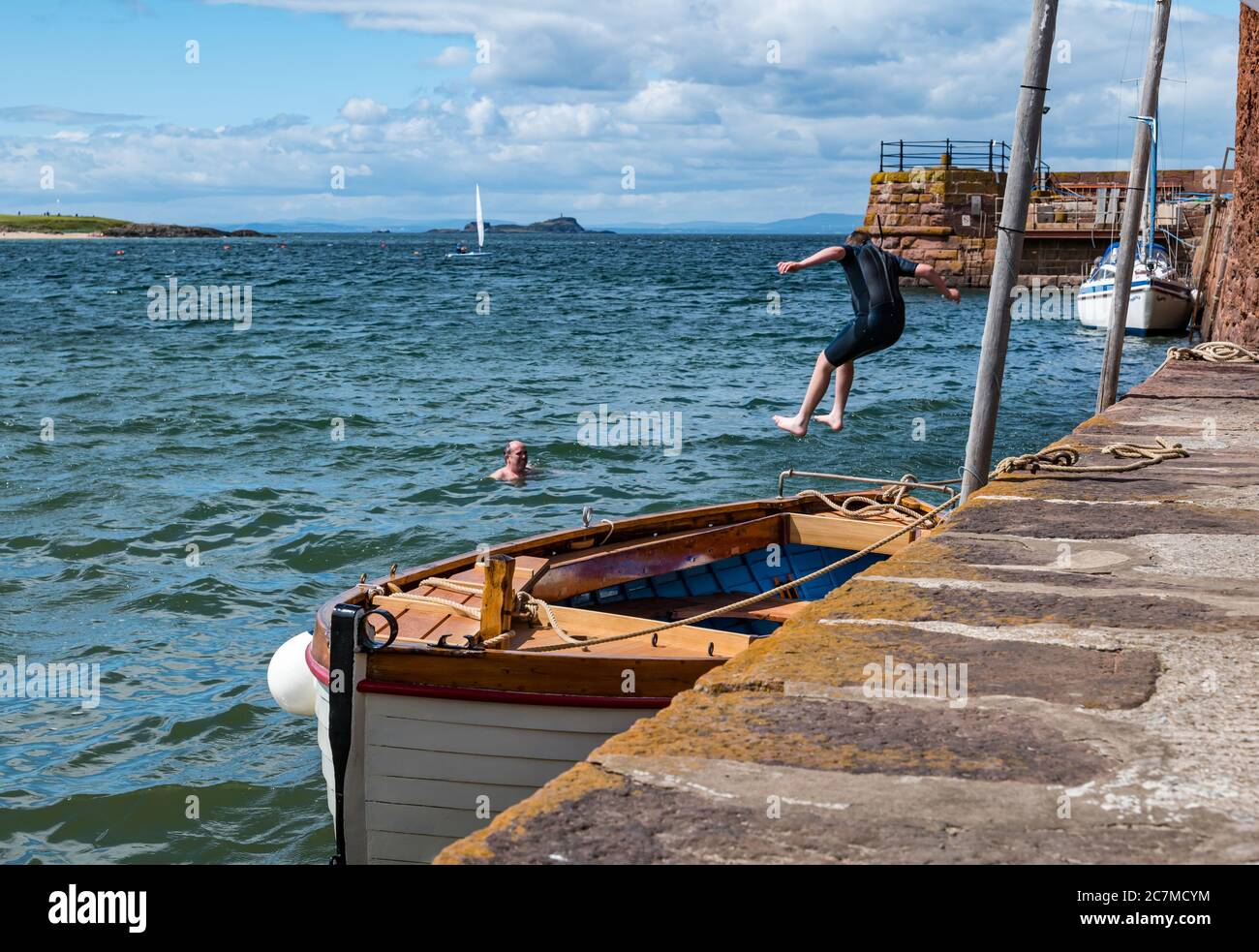North Berwick, East Lothian, Scotland, United Kingdom, 18th July 2020. UK Weather: Summer sunshine in the seaside town. A boy jumps off the harbour wall into the Firth of Forth in West Bay Stock Photo