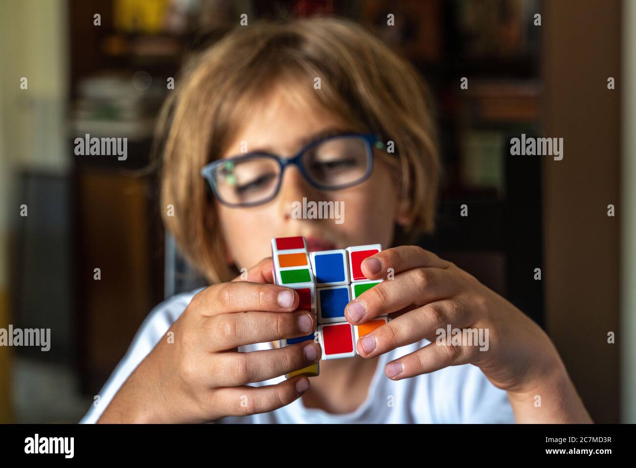 child with glasses trying to solve the Rubik's cube Stock Photo