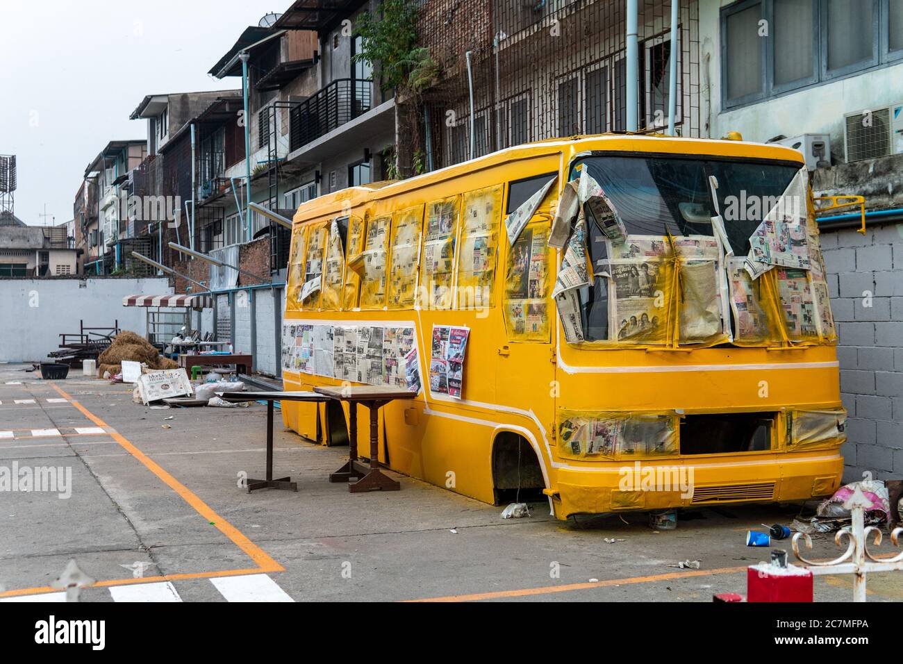 A yellow school bus without tires and in ruin in a parking lot with newspapers on side Stock Photo