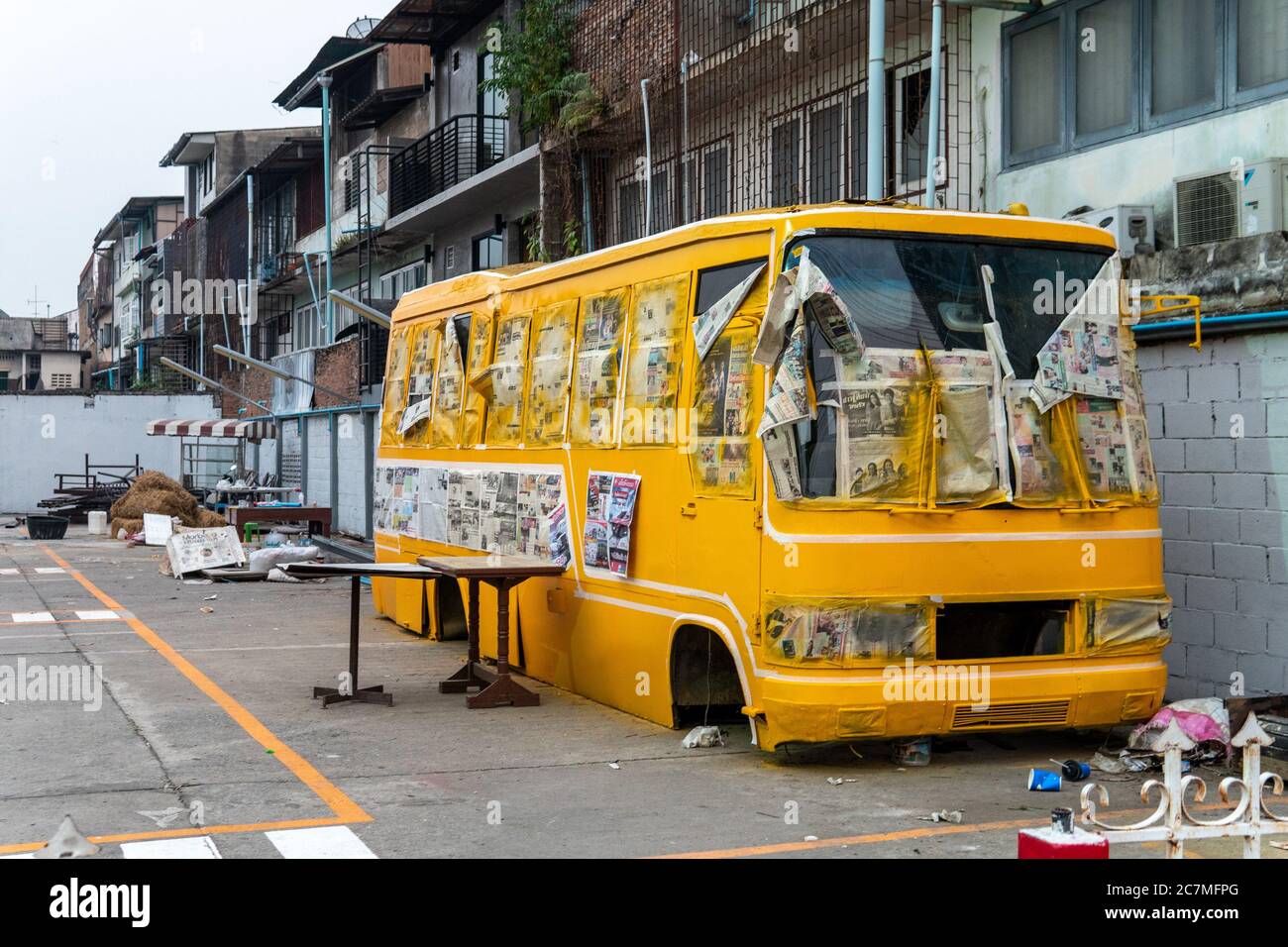 A yellow school bus without tires and in ruin in a parking lot with newspapers on side Stock Photo