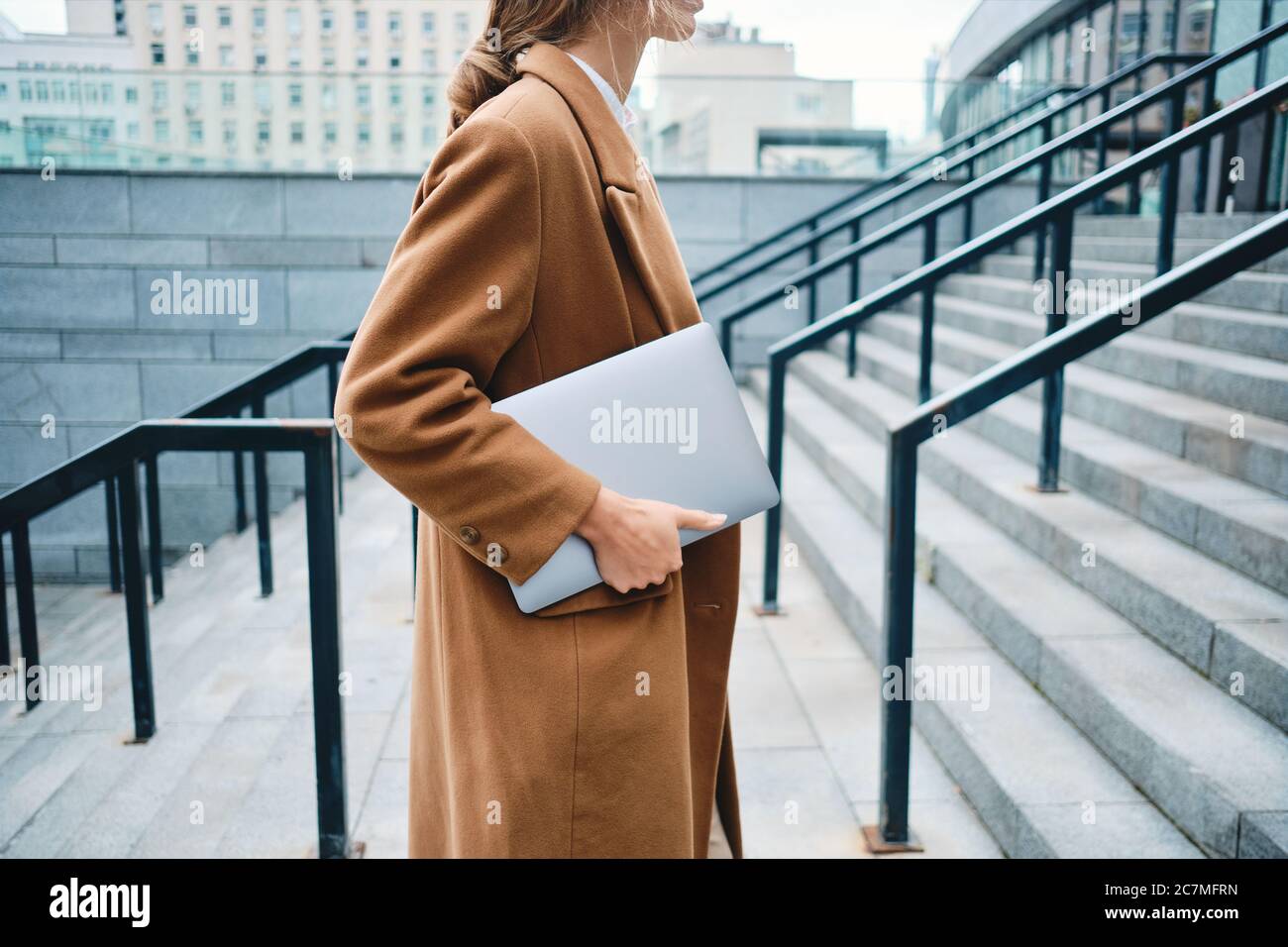 Close up stylish businesswoman in coat with laptop on street Stock Photo