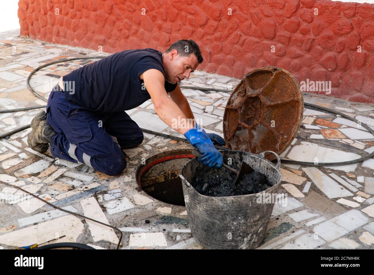 July 13, 2020. Granada. Spain: Worker cleans the drains hatch and removes dirt and debris from the sewer. Plumber cleans the sewer Stock Photo