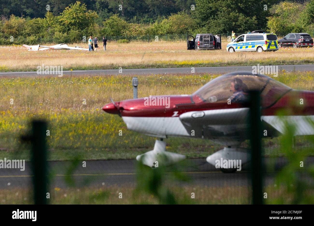 Hangelar, Germany. 18th July, 2020. A crashed glider is lying on the airfield Hangelar near Bonn, while in the foreground a sports plane rolls by. A 17-year-old glider pilot has crashed on the airfield and has been seriously injured. A spokesperson for the fire department said that the accident probably happened during take-off. Credit: Thomas Banneyer/dpa/Alamy Live News Stock Photo