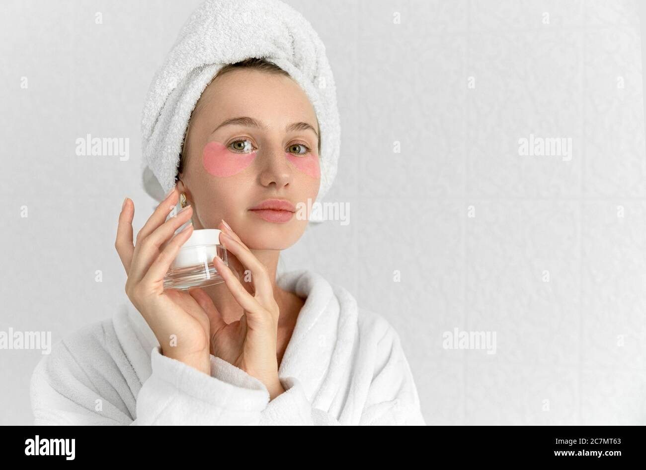 Blonde cute young woman with pink eye patches in white bathroom Stock