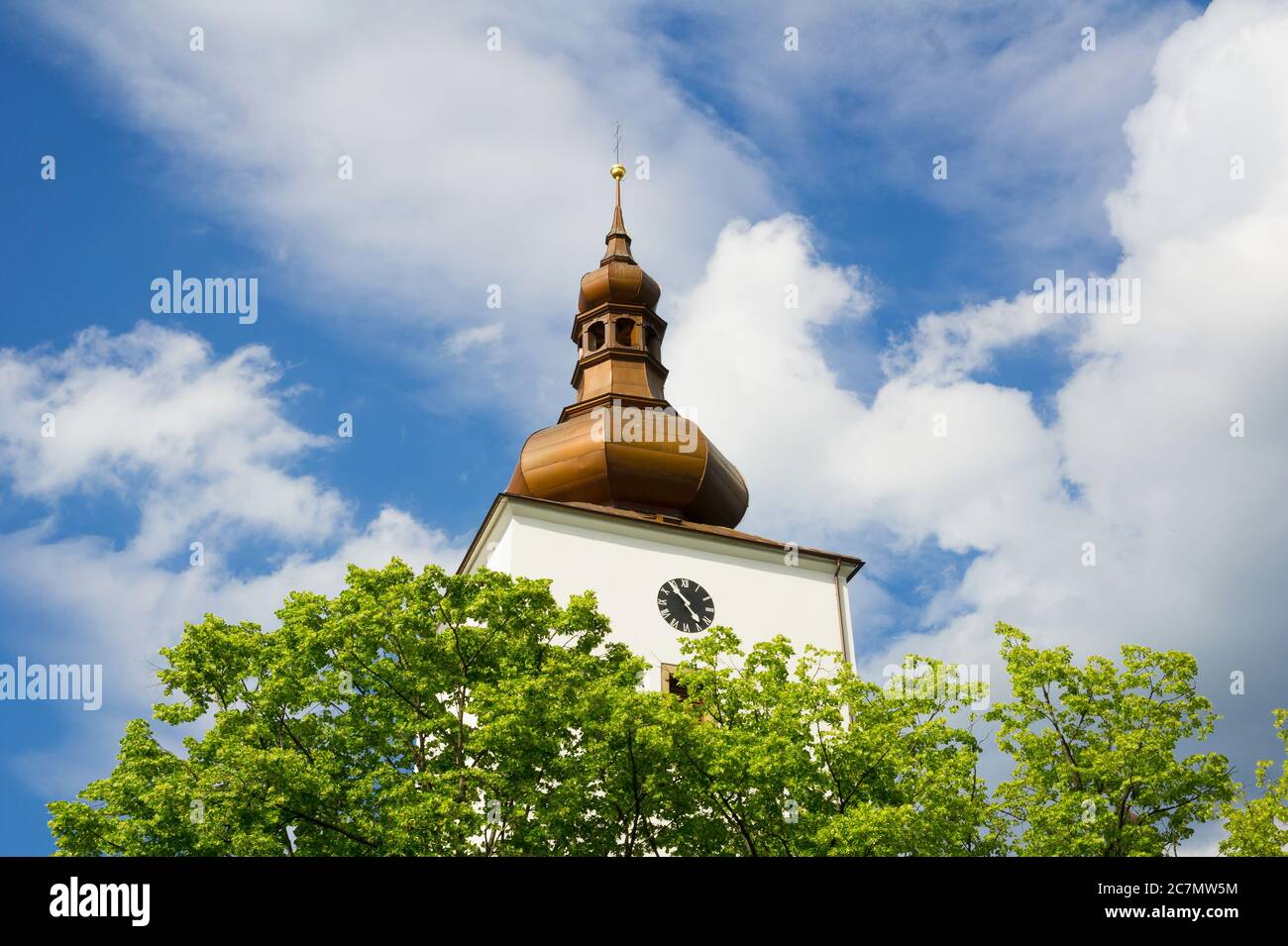 Detail of old historical architecture - baroque tower with cupola, spire and clock. In front of building is green tree during spring or summer Stock Photo